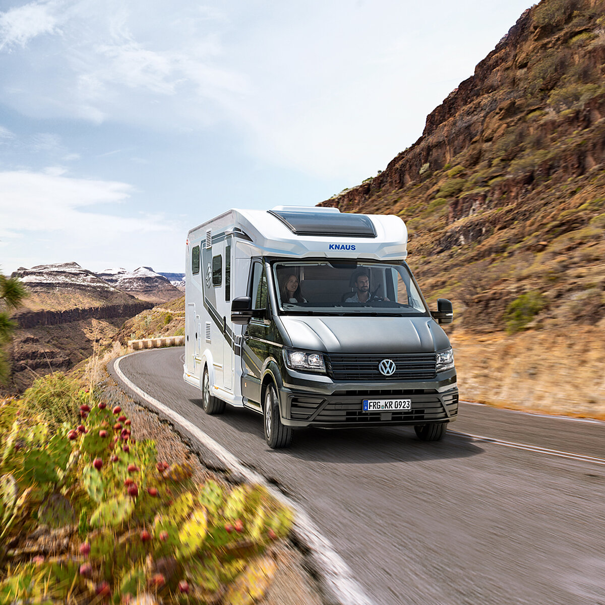 Ein teilintegriertes Wohnmobil fährt auf einer Straße durch eine Berglandschaft.