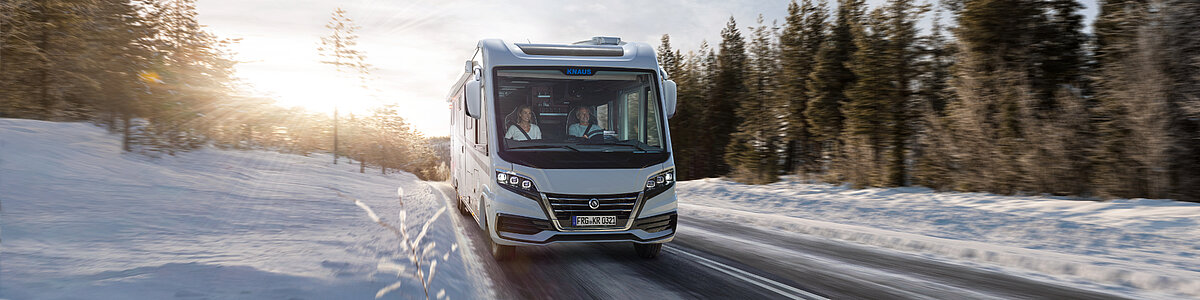 Ein weißes Wohnmobil fährt durch eine Winterlandschaft.