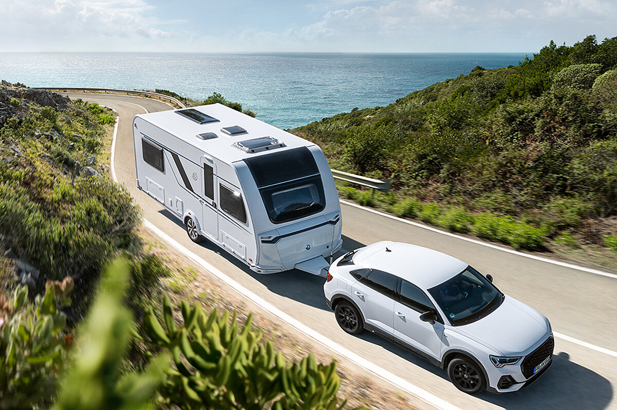 Konfigurieren Sie Ihren Wohnwagen im Knaus-Konfigurator. Ein SUV zieht einen Wohnwagen von Knaus eine Straße entlang.