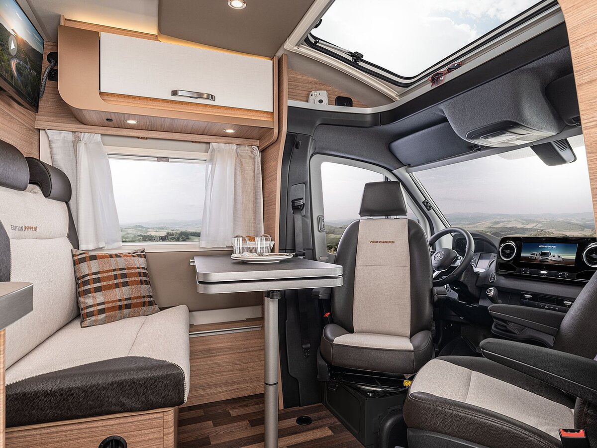 Der Innenraum eines Wohnmobils zur Sitzecke mit Tisch und den umgedrehten Fahrersitzen im Fahrerhaus